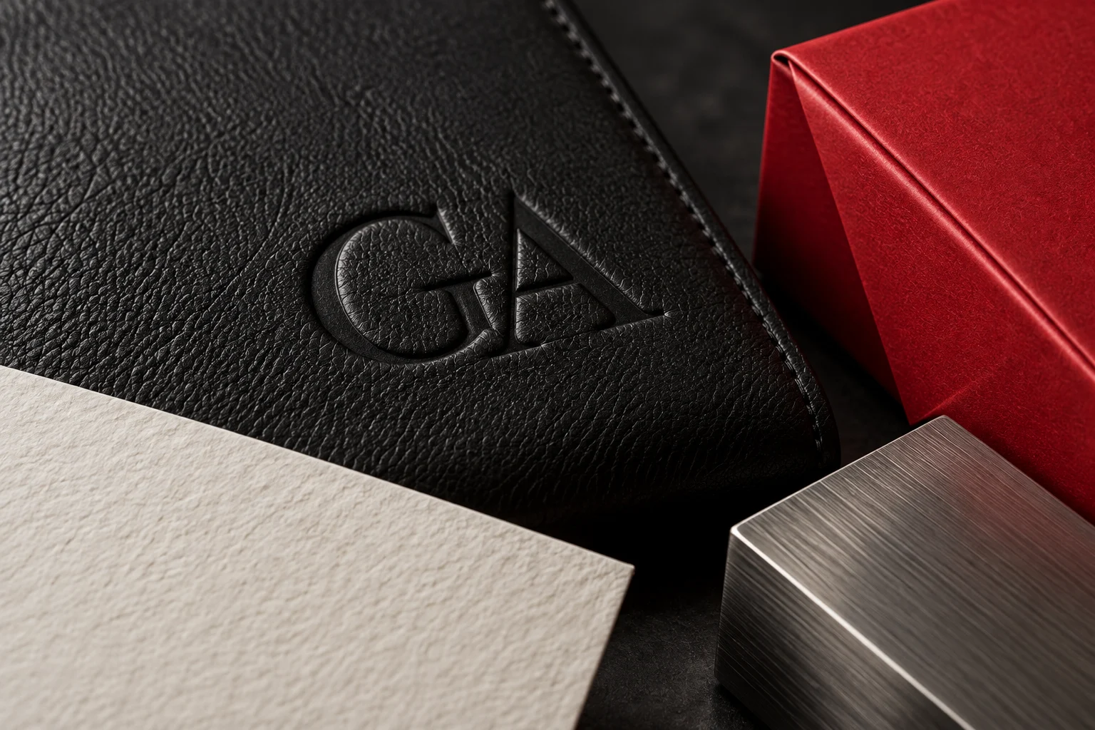 Illustrative close-up of debossed leather, textured paper, red packaging and brushed metal